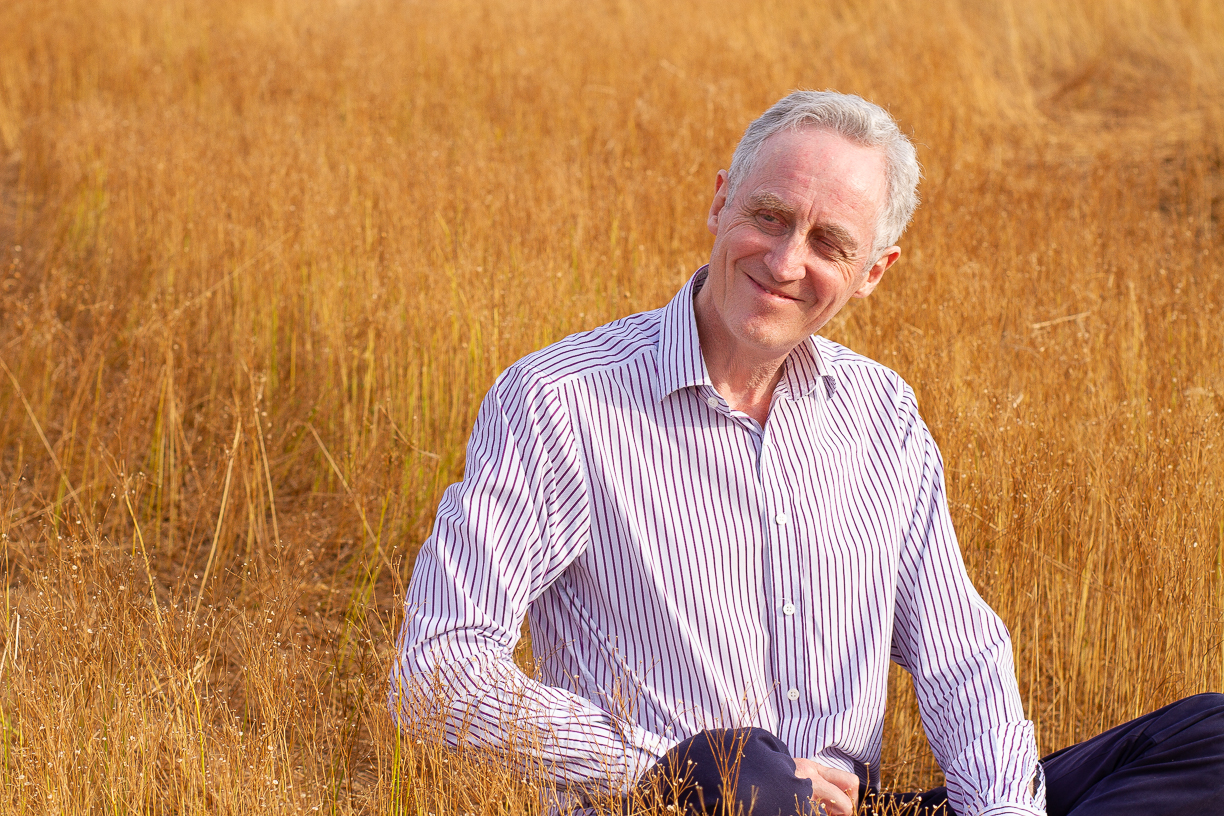 Coach sitting in a grassy sunlit field, smiling and looking to his right