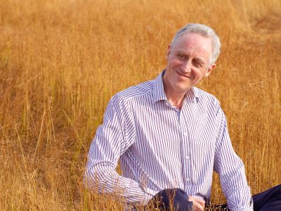 Coach sitting in a grassy sunlit field, smiling and looking to his right