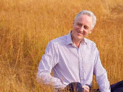 Coach sitting in a grassy sunlit field, smiling and looking to his right