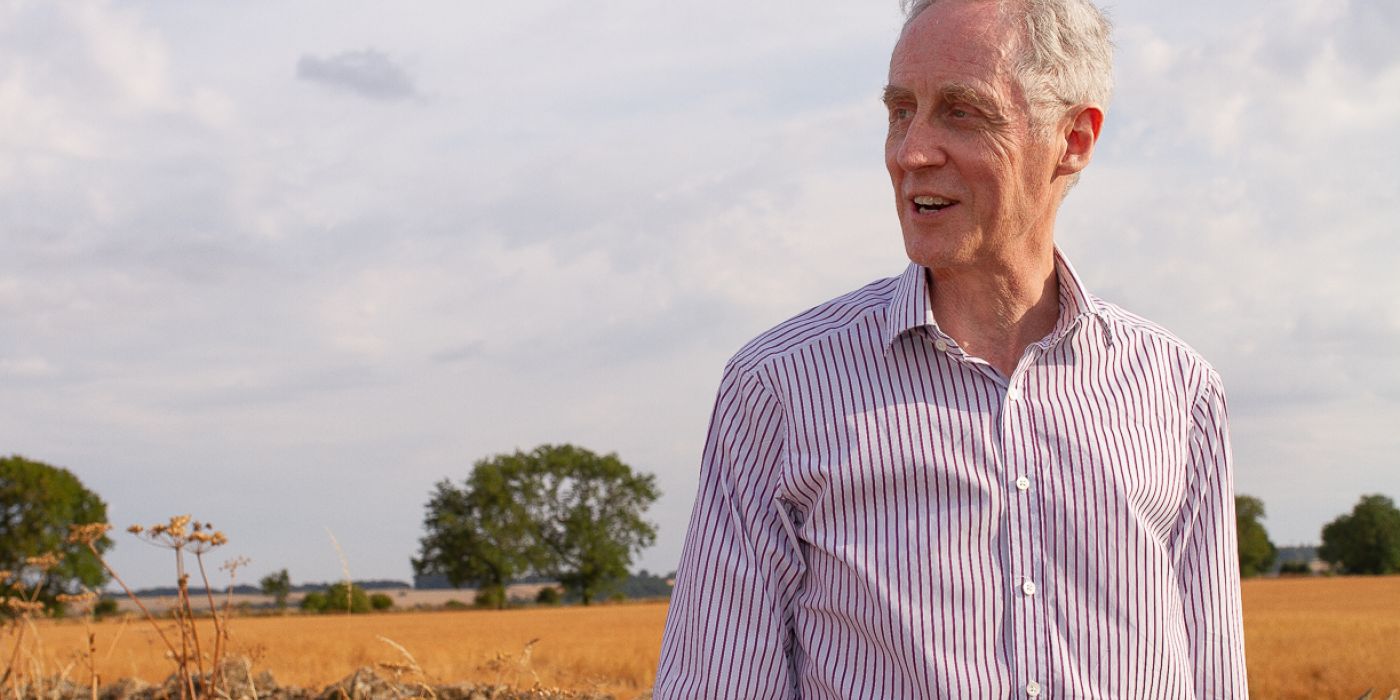 Man standing, looking to his right in front of wheat field and trees